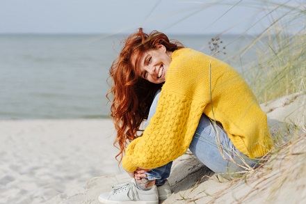 fata aflata la mare care poarta un pulover galben si blugi